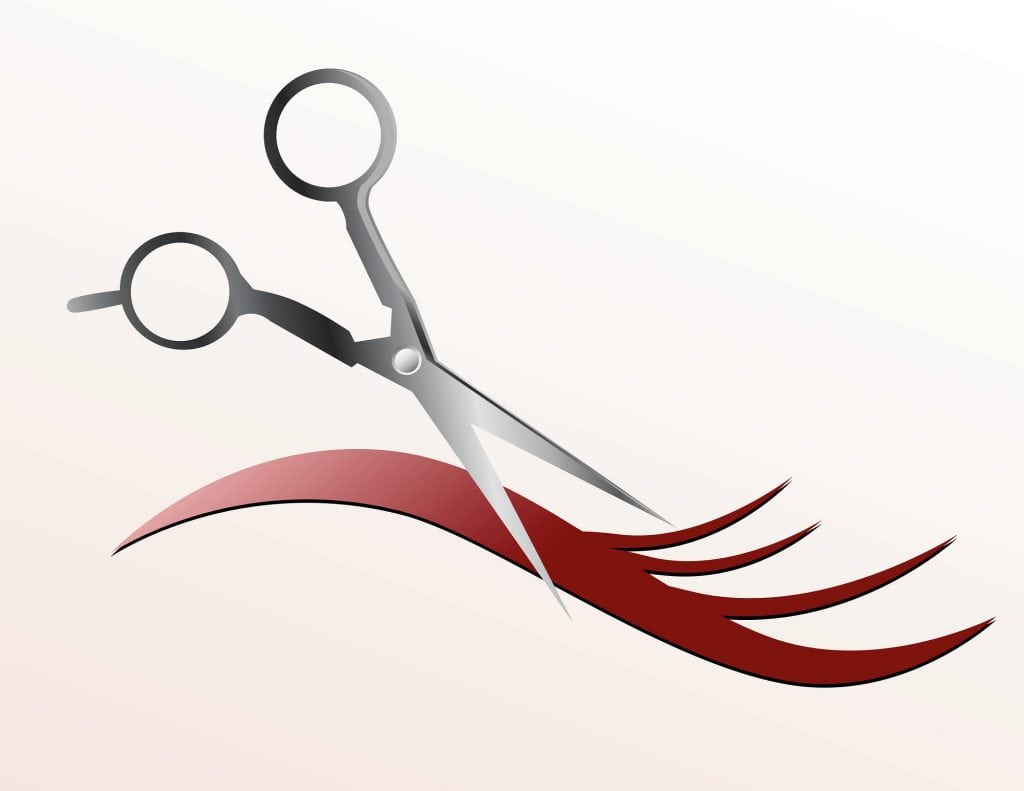 Scissors are cutting a strand of flowing hair and the background is pink.