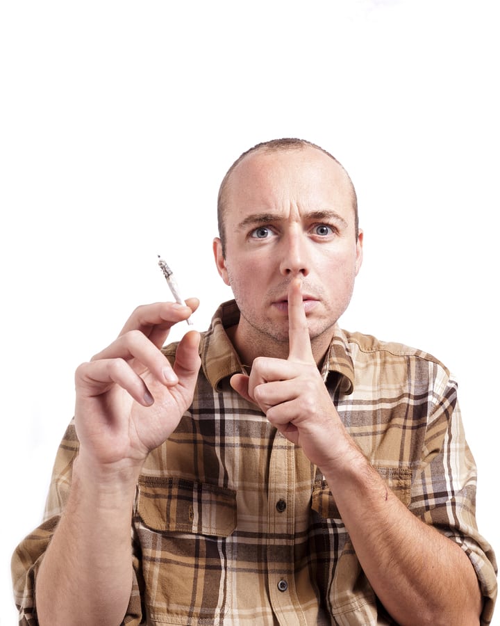 A man gestures to not tell on him while caught smoking a joint.